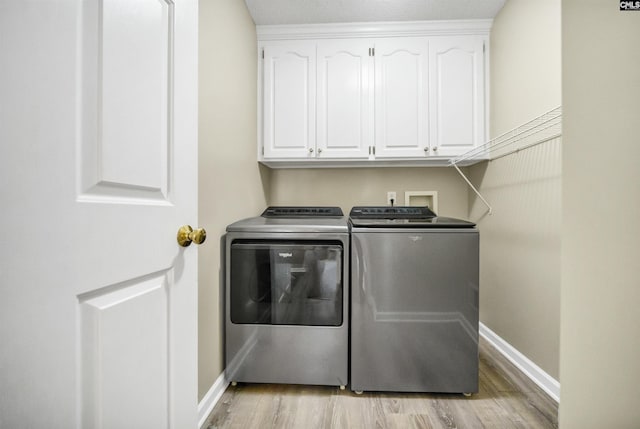 laundry area featuring separate washer and dryer, cabinets, and light wood-type flooring