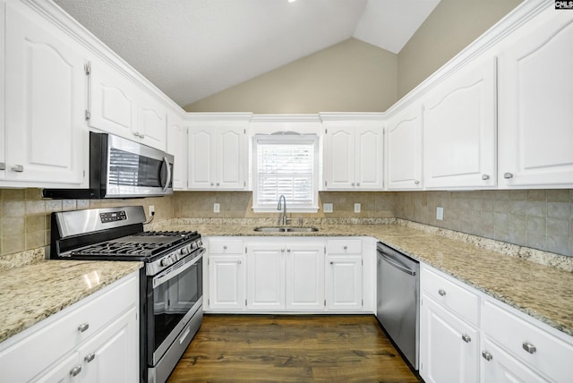 kitchen with sink, white cabinetry, stainless steel appliances, light stone counters, and vaulted ceiling