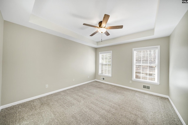 spare room featuring a raised ceiling, ceiling fan, and carpet