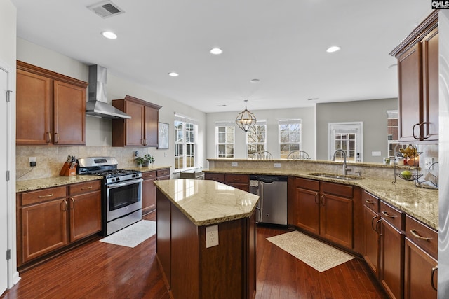 kitchen with decorative light fixtures, sink, kitchen peninsula, stainless steel appliances, and wall chimney exhaust hood