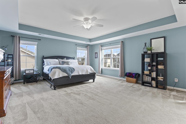 bedroom with light colored carpet, ceiling fan, and a tray ceiling