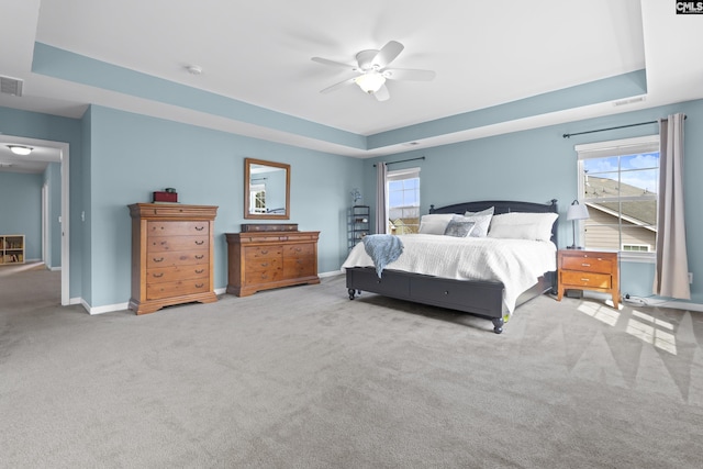 carpeted bedroom featuring multiple windows, ceiling fan, and a tray ceiling