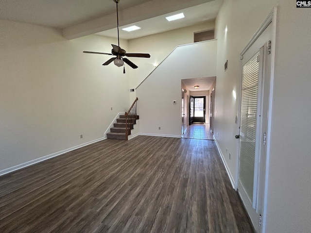 unfurnished living room featuring dark wood-type flooring, ceiling fan, and a high ceiling