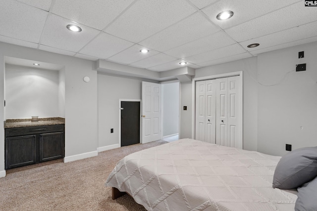 bedroom with a closet, light carpet, and a drop ceiling