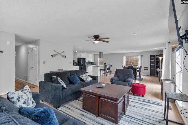 living room with ceiling fan, light hardwood / wood-style flooring, and a textured ceiling