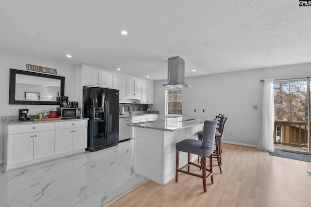 kitchen with stone counters, island range hood, white cabinetry, a kitchen bar, and stainless steel appliances