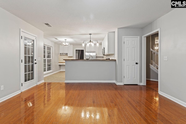 unfurnished living room with an inviting chandelier, sink, a textured ceiling, and light wood-type flooring