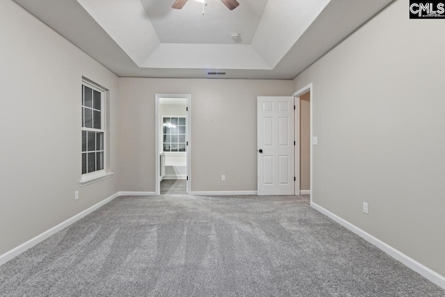 unfurnished bedroom featuring ceiling fan, a tray ceiling, carpet flooring, and ensuite bath