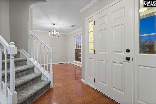 foyer entrance featuring a notable chandelier, wood-type flooring, ornamental molding, and a textured ceiling