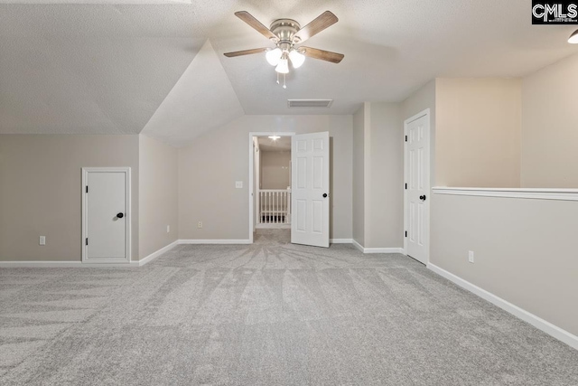 additional living space with ceiling fan, lofted ceiling, light colored carpet, and a textured ceiling