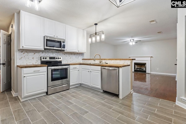 kitchen with appliances with stainless steel finishes, hanging light fixtures, backsplash, white cabinets, and kitchen peninsula