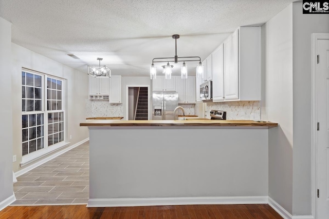 kitchen with appliances with stainless steel finishes, pendant lighting, white cabinets, and kitchen peninsula