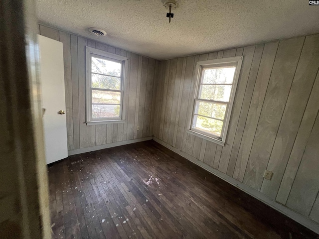 spare room with a textured ceiling, dark hardwood / wood-style flooring, and wood walls