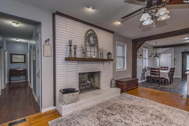 living room with a brick fireplace, hardwood / wood-style flooring, a textured ceiling, and ceiling fan