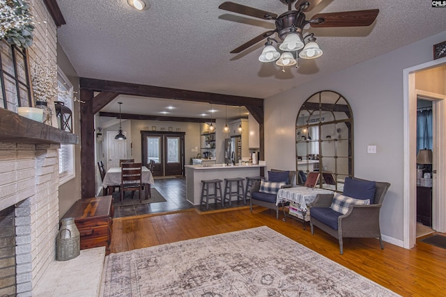 living room featuring a brick fireplace, hardwood / wood-style floors, a textured ceiling, and french doors