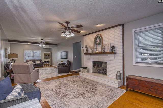 living room with a brick fireplace, ceiling fan, a textured ceiling, and light wood-type flooring