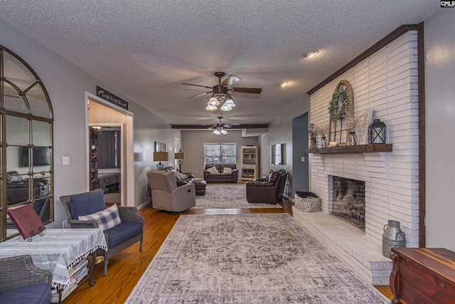 living room with a brick fireplace, wood-type flooring, a textured ceiling, and ceiling fan