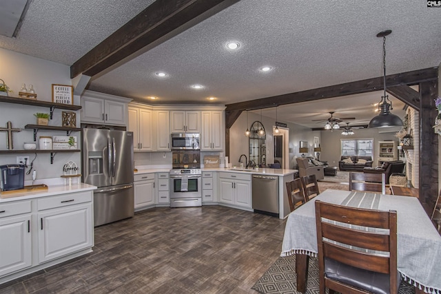 kitchen with appliances with stainless steel finishes, decorative light fixtures, white cabinets, beam ceiling, and a textured ceiling