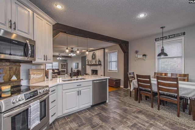 kitchen featuring sink, white cabinetry, hanging light fixtures, stainless steel appliances, and a brick fireplace