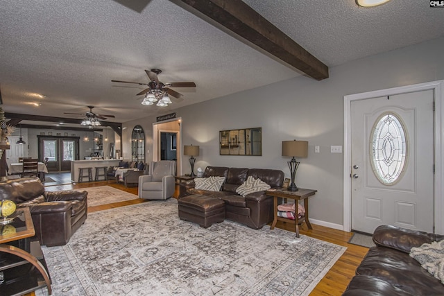 living room featuring ceiling fan, a textured ceiling, light hardwood / wood-style flooring, and beamed ceiling