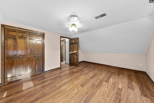 unfurnished bedroom featuring lofted ceiling, hardwood / wood-style flooring, and a textured ceiling