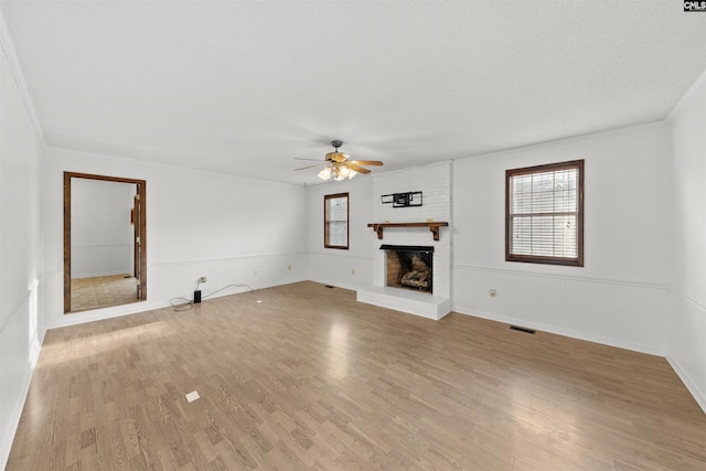 unfurnished living room featuring ceiling fan, a brick fireplace, a textured ceiling, and light wood-type flooring