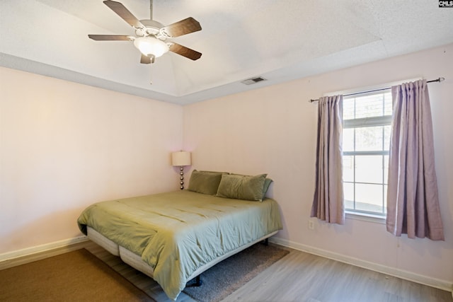 bedroom with ceiling fan, a tray ceiling, and light hardwood / wood-style flooring