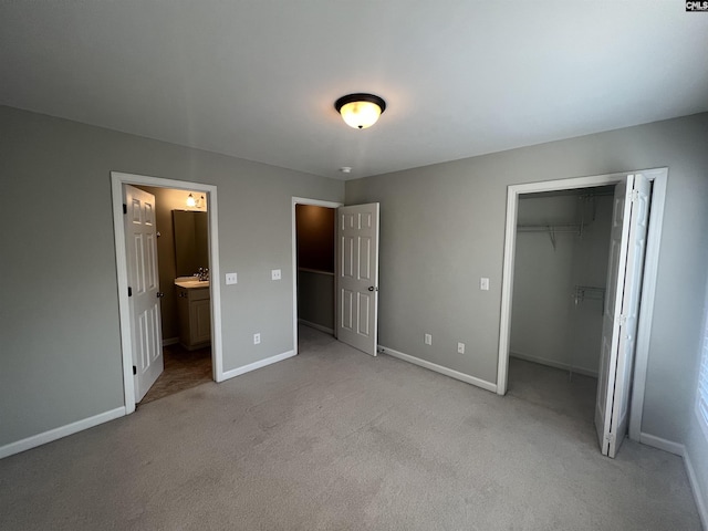 unfurnished bedroom with sink, a walk in closet, light colored carpet, ensuite bath, and a closet