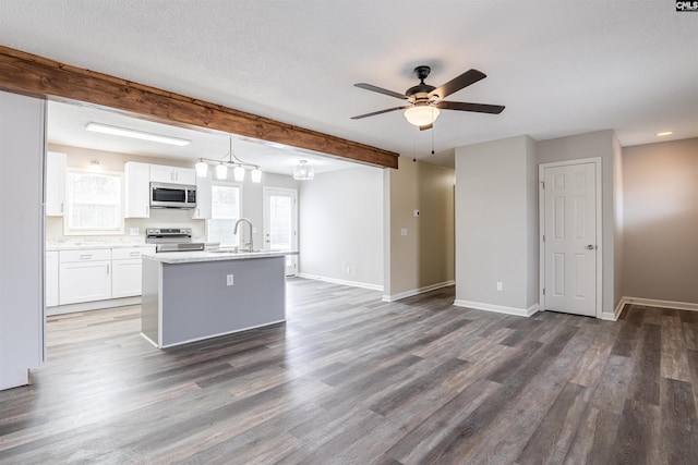 kitchen featuring pendant lighting, white cabinetry, stainless steel appliances, a center island with sink, and beam ceiling