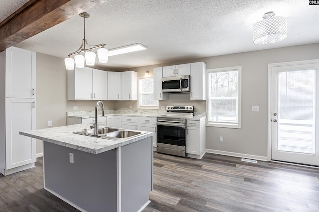 kitchen featuring sink, appliances with stainless steel finishes, a kitchen island with sink, white cabinets, and decorative light fixtures