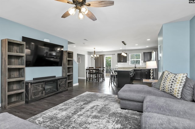 living room featuring a fireplace, ceiling fan with notable chandelier, dark wood-type flooring, and sink