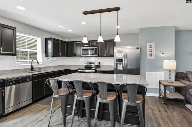 kitchen with sink, appliances with stainless steel finishes, hanging light fixtures, backsplash, and a center island