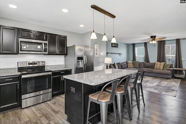 kitchen featuring a kitchen island, appliances with stainless steel finishes, pendant lighting, tasteful backsplash, and a breakfast bar area