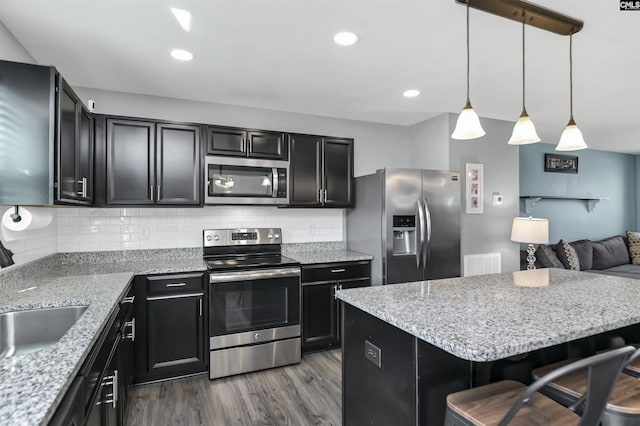 kitchen with appliances with stainless steel finishes, hanging light fixtures, hardwood / wood-style floors, a kitchen breakfast bar, and decorative backsplash