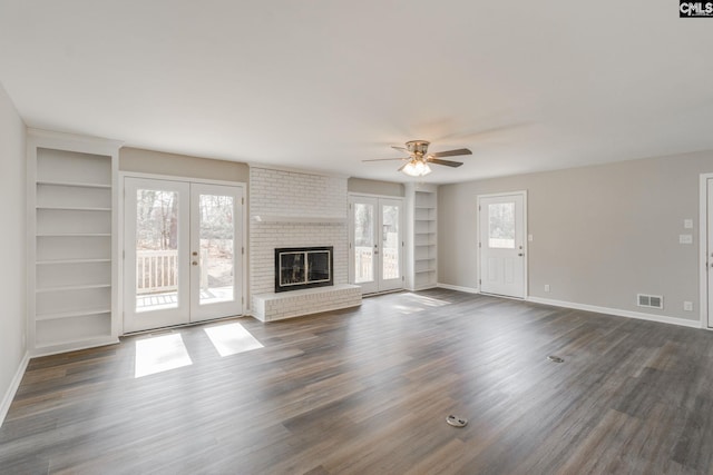 unfurnished living room featuring french doors, built in shelves, a brick fireplace, dark hardwood / wood-style flooring, and ceiling fan