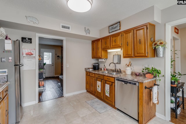 kitchen with light stone counters, sink, a textured ceiling, and appliances with stainless steel finishes