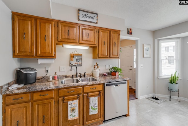 kitchen featuring light stone counters, sink, stainless steel dishwasher, and a textured ceiling