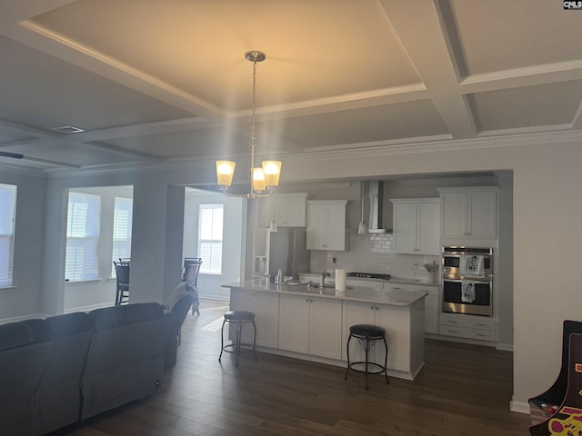 kitchen with a breakfast bar, a kitchen island with sink, hanging light fixtures, white cabinets, and wall chimney exhaust hood