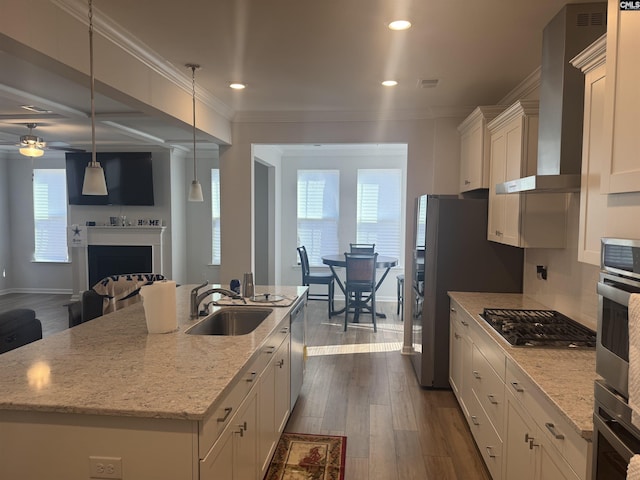 kitchen featuring sink, decorative light fixtures, an island with sink, and wall chimney range hood