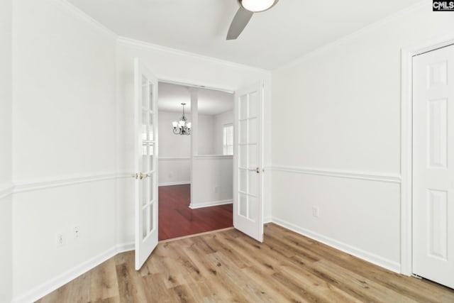 empty room with crown molding, ceiling fan with notable chandelier, hardwood / wood-style floors, and french doors