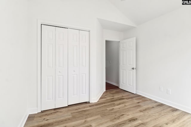 unfurnished bedroom featuring vaulted ceiling, a closet, and light wood-type flooring