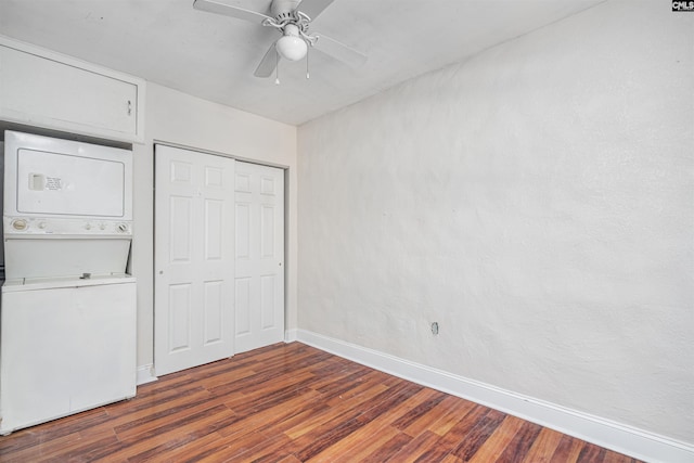 unfurnished bedroom with stacked washer / drying machine, dark wood-type flooring, ceiling fan, and a closet