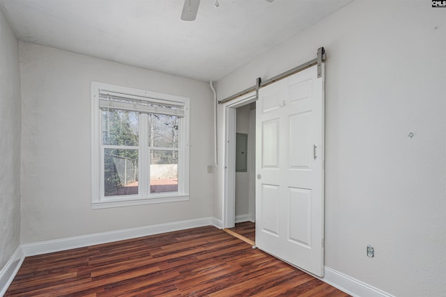 unfurnished bedroom with a barn door, dark wood-type flooring, electric panel, and ceiling fan