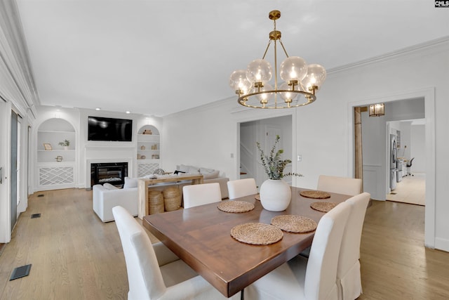 dining room with crown molding, built in shelves, a notable chandelier, and light hardwood / wood-style flooring