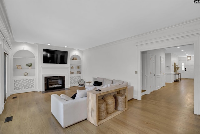 living room with crown molding, built in features, and light hardwood / wood-style flooring