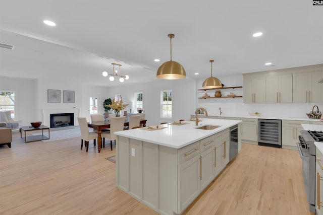 kitchen with appliances with stainless steel finishes, decorative light fixtures, sink, beverage cooler, and a center island with sink