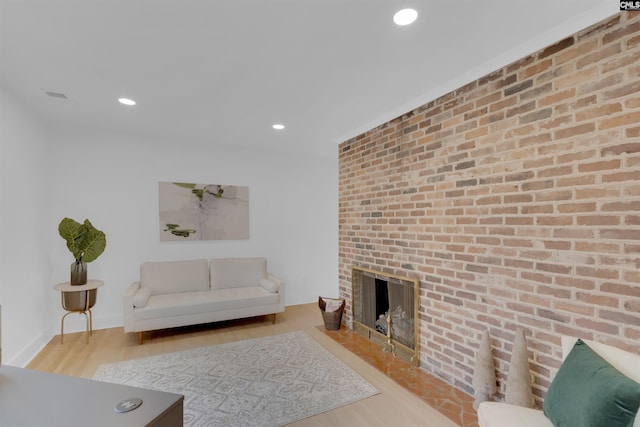 living room with brick wall, a fireplace, and light hardwood / wood-style flooring