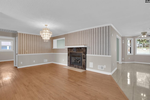 unfurnished living room featuring crown molding, ceiling fan with notable chandelier, a fireplace, and light hardwood / wood-style floors