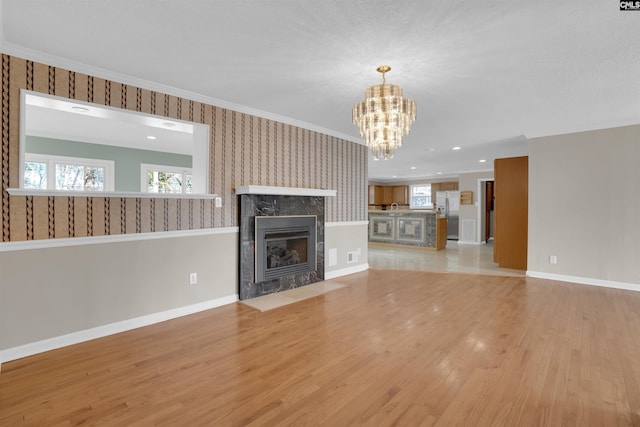 unfurnished living room featuring a chandelier, ornamental molding, a tiled fireplace, and light wood-type flooring