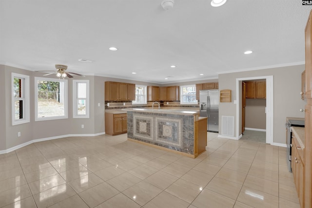 kitchen featuring crown molding, appliances with stainless steel finishes, a center island with sink, and light tile patterned flooring